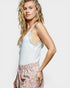 Woman wearing a white lace camisole and colorful pants on a light background