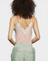 Person wearing a pink lace camisole and green pants with floral details on a light gray background