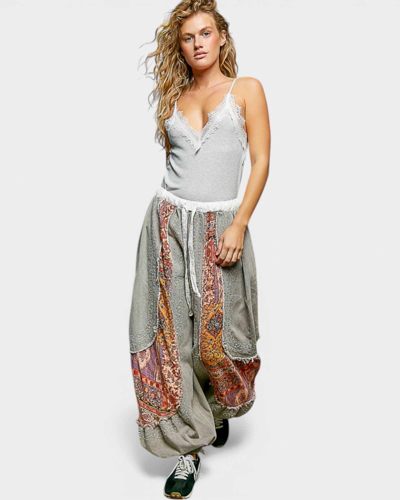 Woman wearing a gray tank top and patterned harem pants on a white background