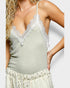 Woman wearing a green tank top with lace details on a light gray background