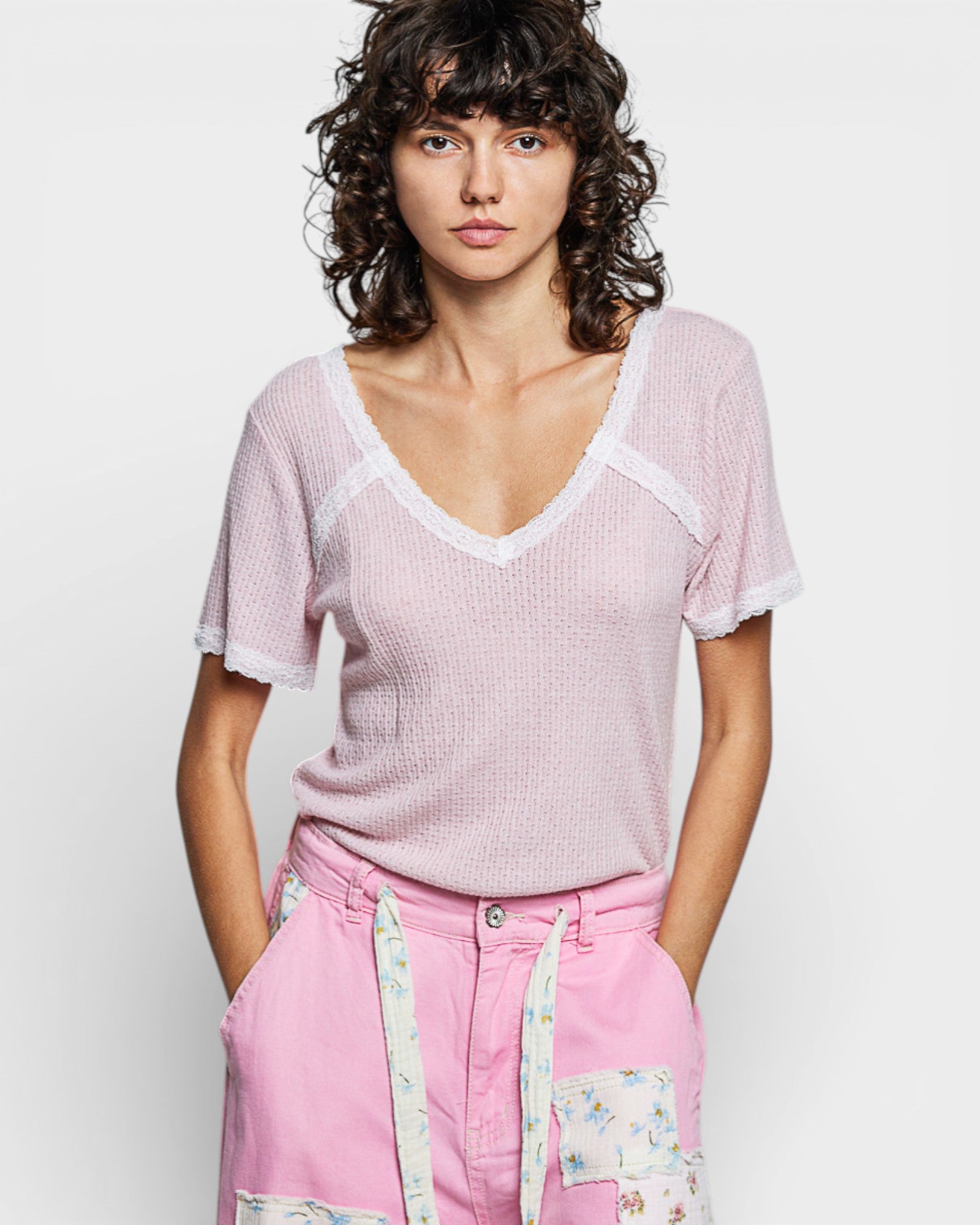 Woman wearing a pink textured top and pink pants with floral patches on a white background
