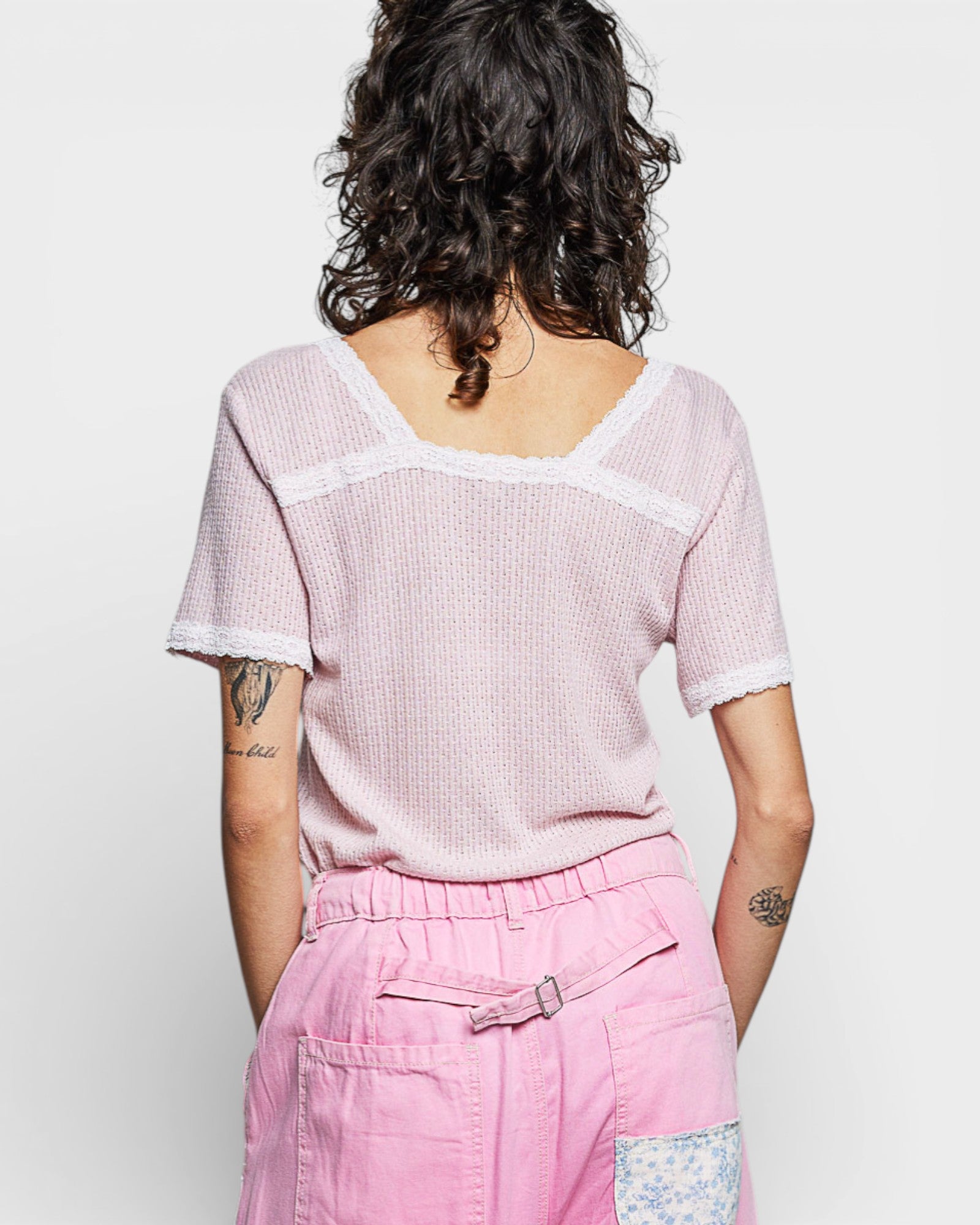 Person wearing a pink textured top and pink pants against a white background