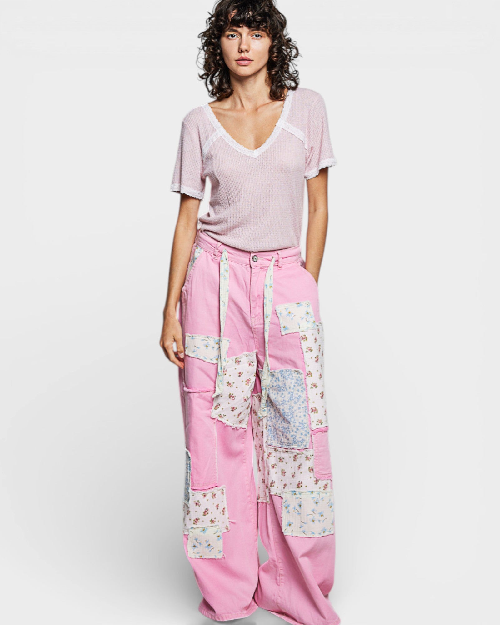 Woman wearing a light pink top and patchwork pink pants on a white background