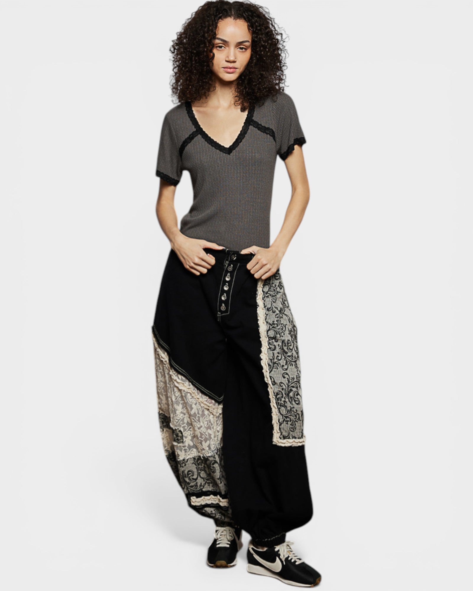 Woman wearing a gray top and black patterned pants on a white background