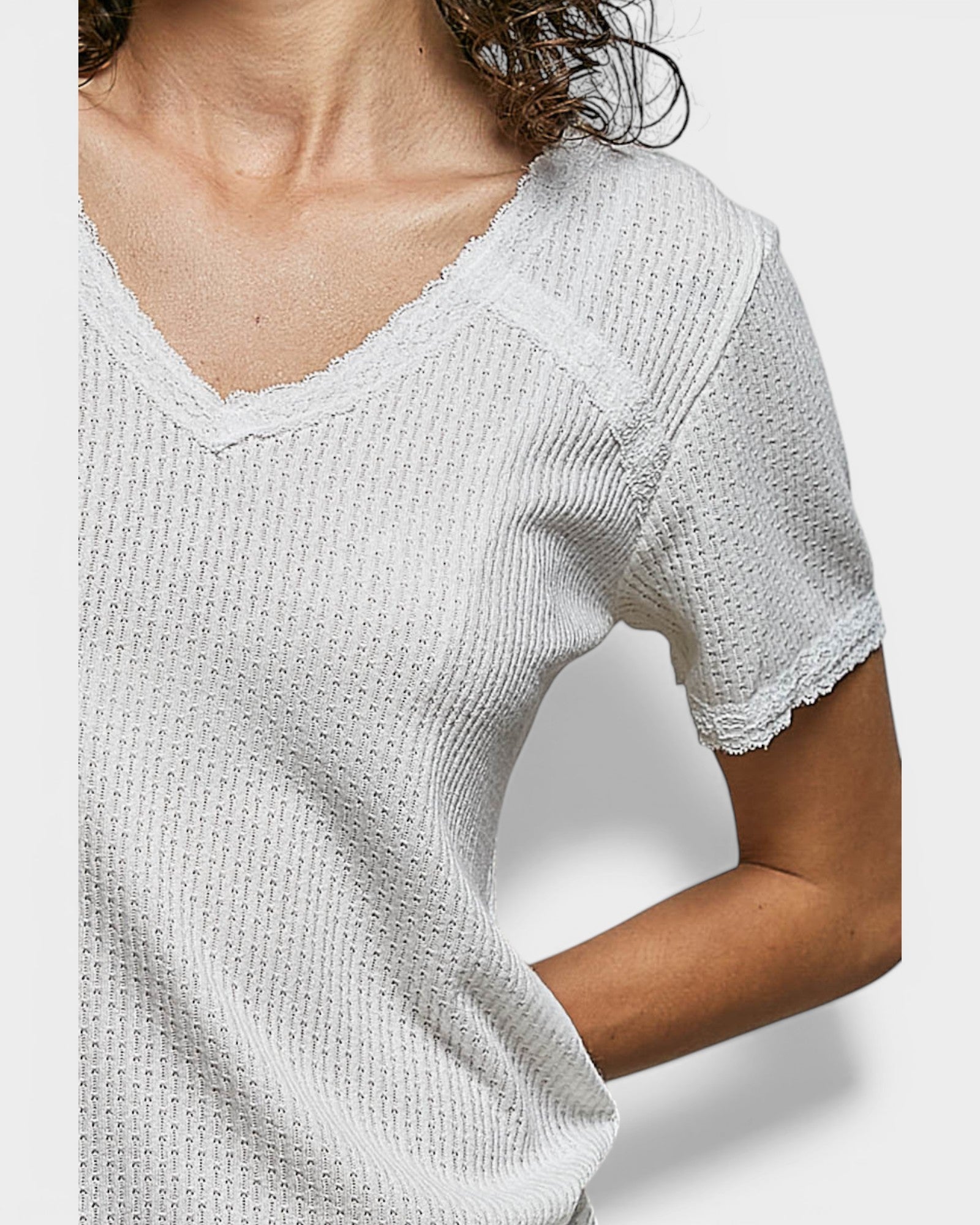 White textured short-sleeve top worn by a person on a light gray background