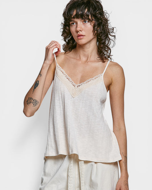 Woman wearing a light-colored lace-trimmed top against a plain background