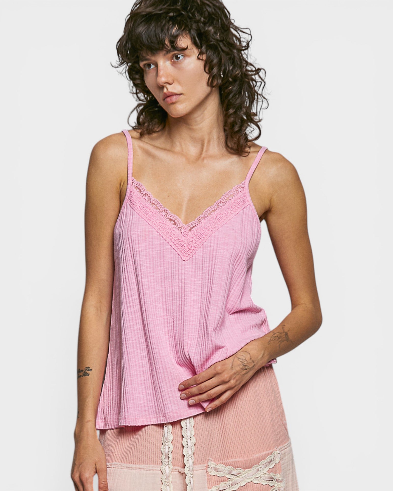 Woman wearing a pink lace-trimmed top against a plain background