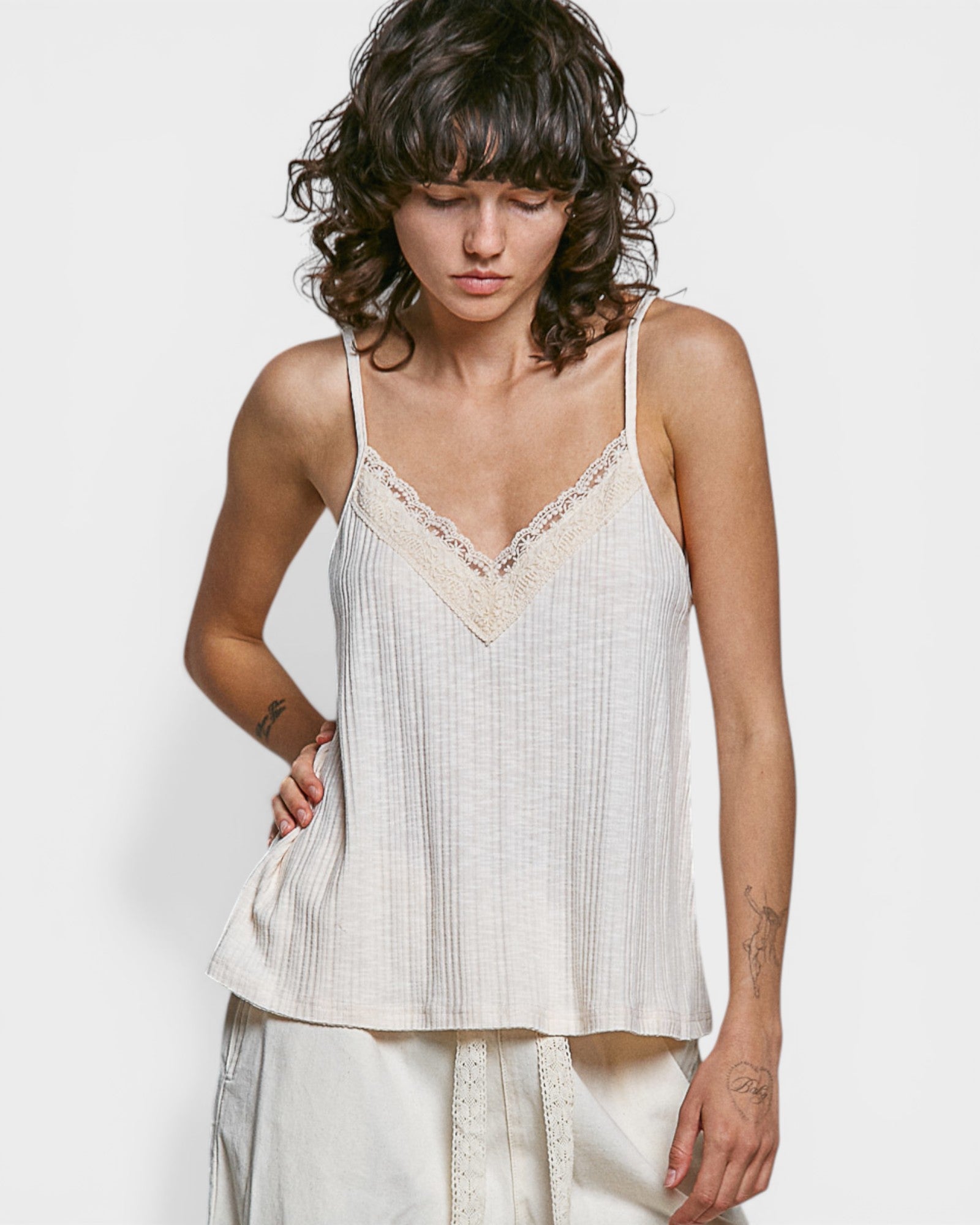 Woman wearing a white lace-trimmed top against a plain background