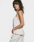 Woman wearing a light-colored sleeveless top and white pants against a plain background