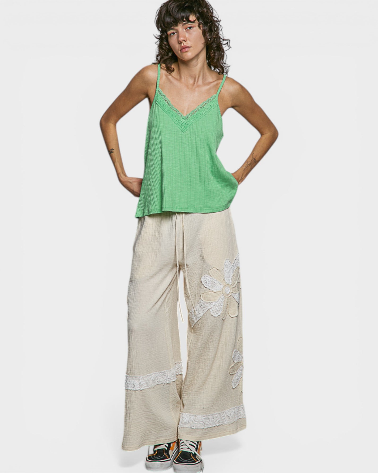 Woman wearing a green top and beige pants with floral embroidery on a white background