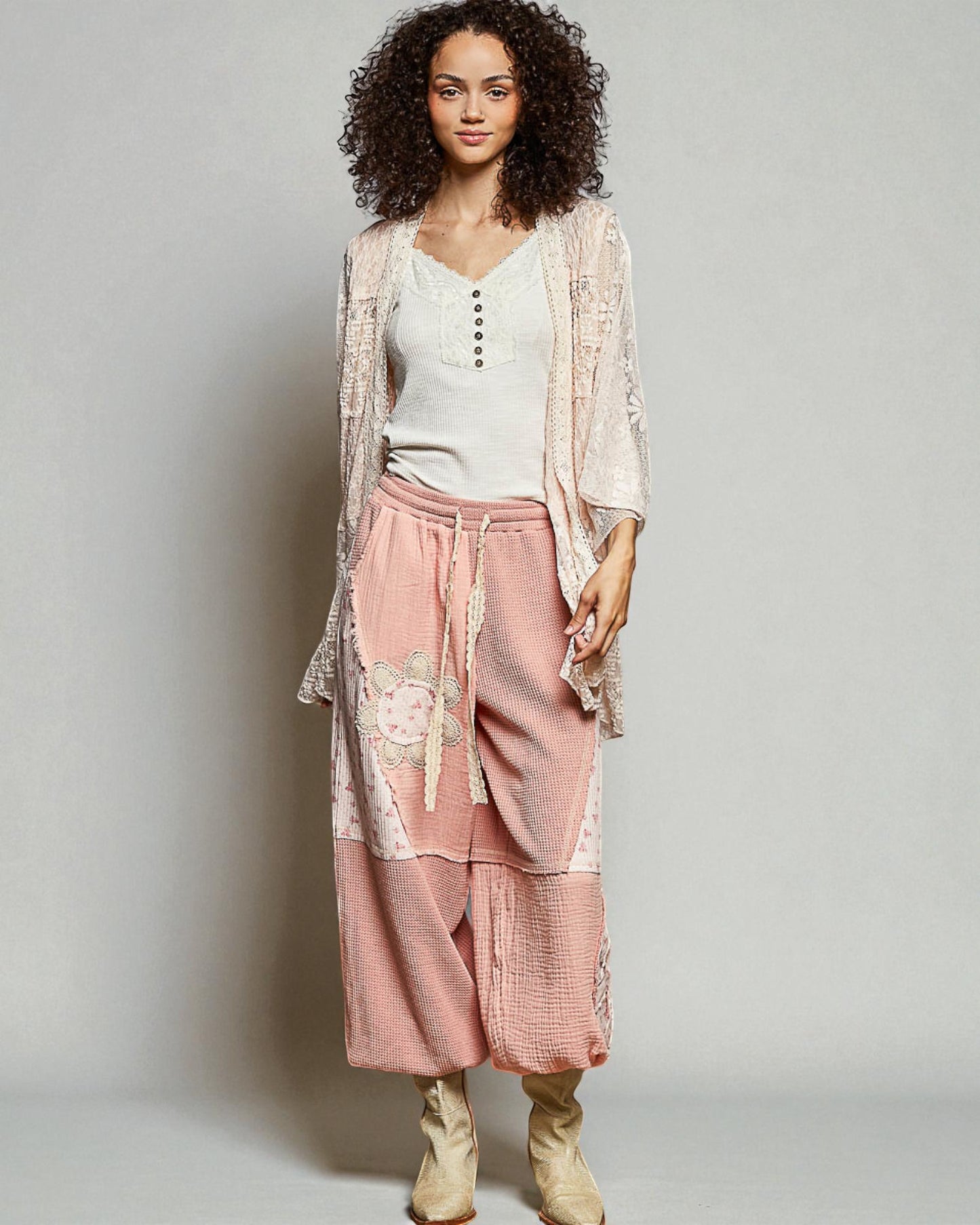 Woman wearing a light pink outfit with a lace cardigan on a plain background