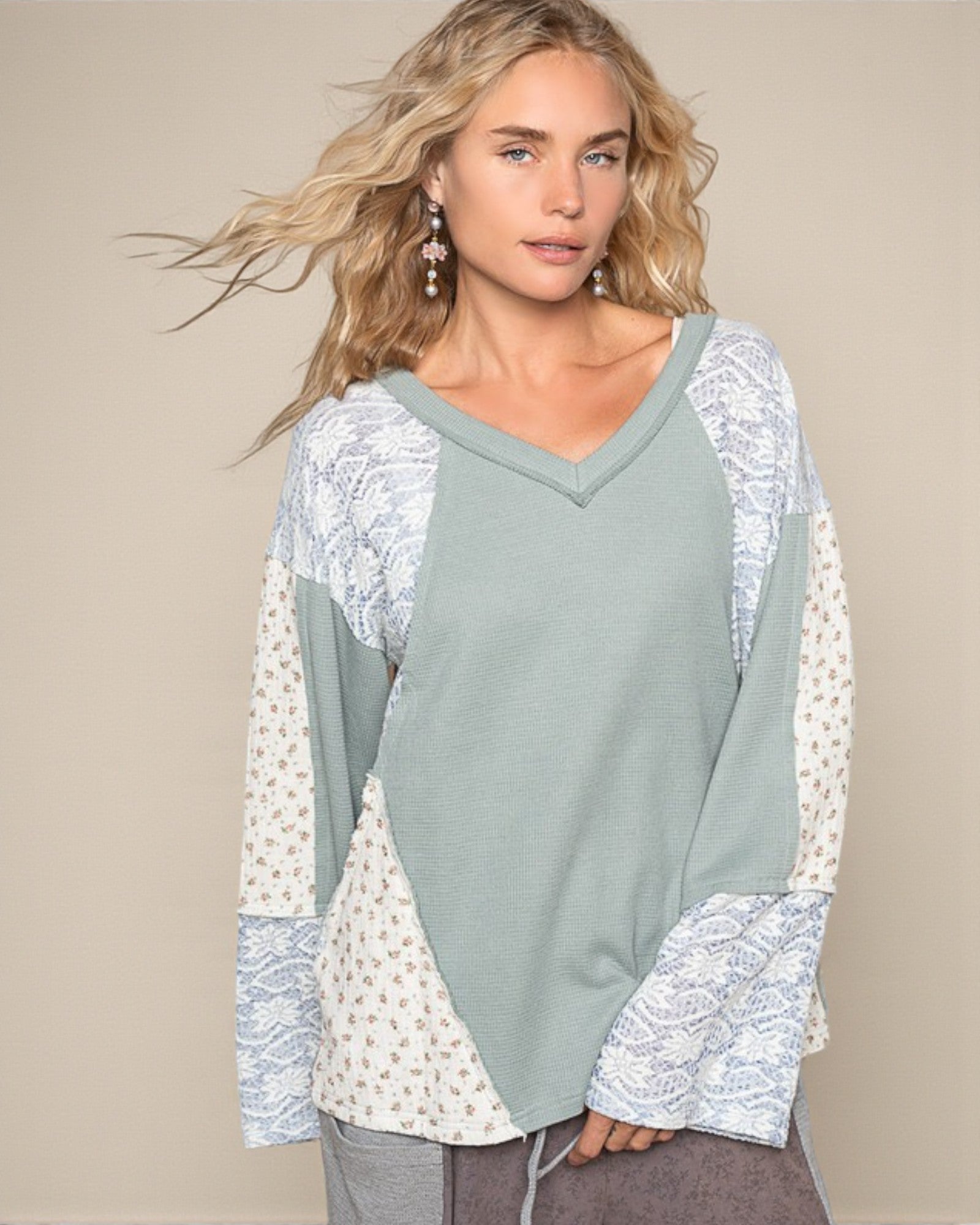 Woman wearing a light green long-sleeve top with lace detailing on a beige background