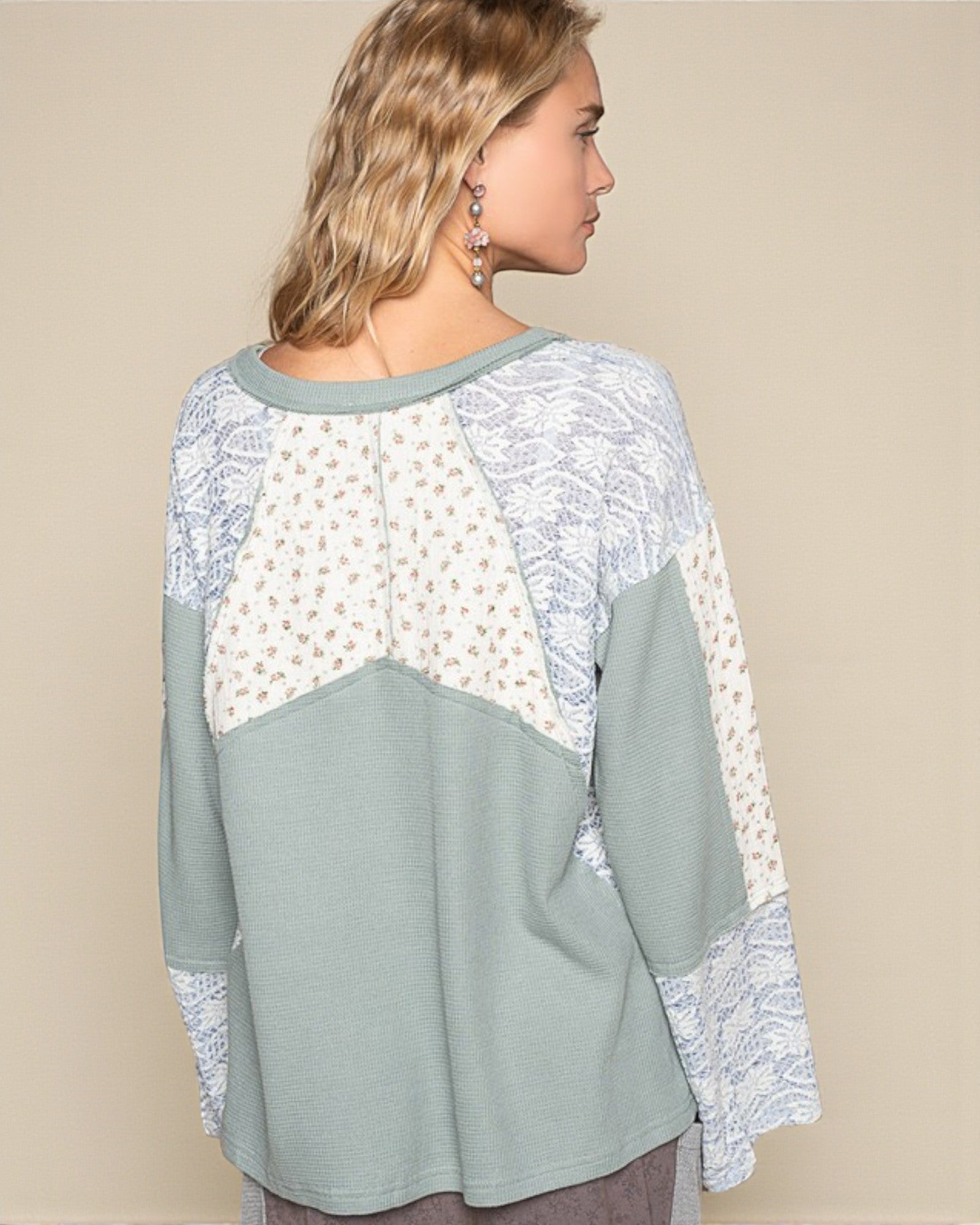 Woman wearing a light blue top with lace sleeves and neckline on a beige background