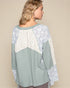 Woman wearing a light blue top with lace sleeves and neckline on a beige background