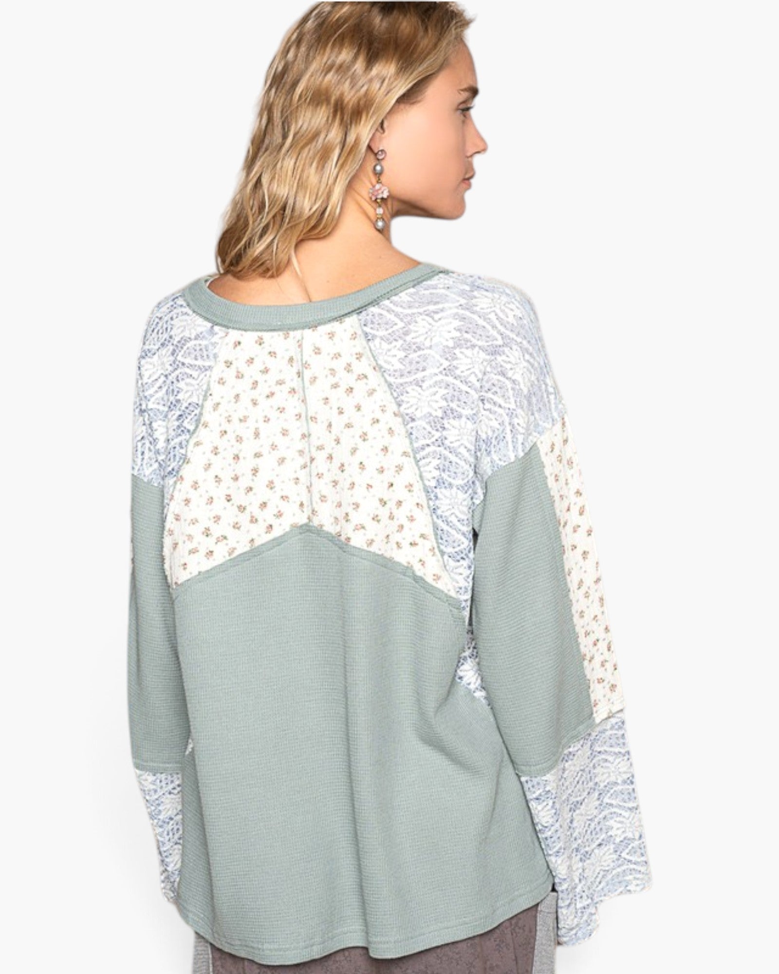A woman shown from the back wearing a color-blocked long-sleeve top with sage green panels, white patterned yoke panels, and matching white lace cuffs, against a plain light gray background.