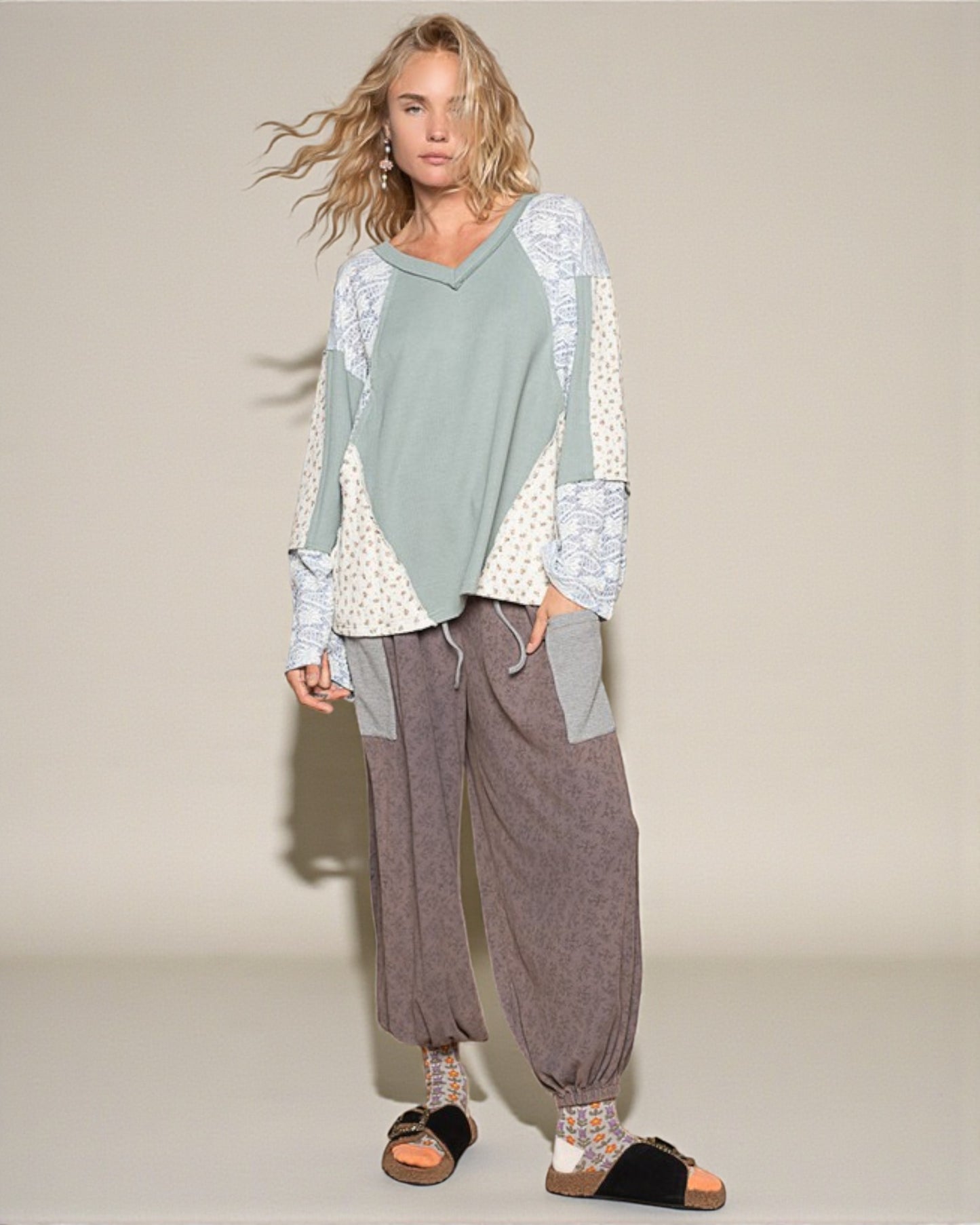 Woman wearing a light green and white patterned top with brown wide-leg pants on a beige background