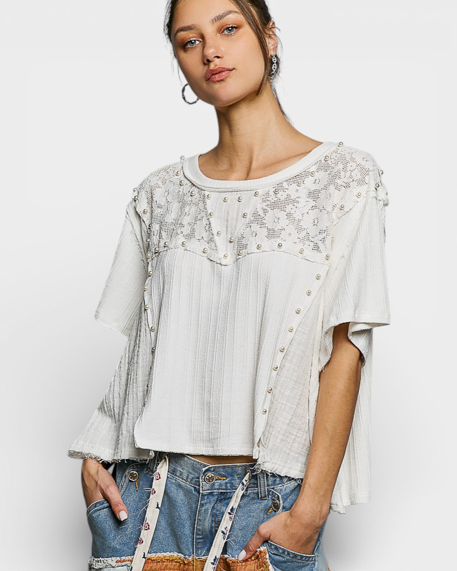 Woman wearing a white lace top and denim shorts on a plain background