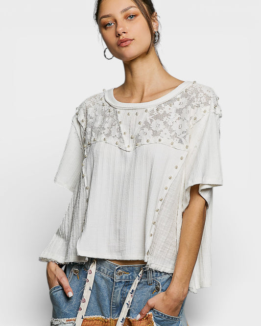 Woman wearing a white lace top and denim shorts on a plain background