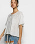 Woman wearing a light-colored blouse with lace details and denim pants on a white background