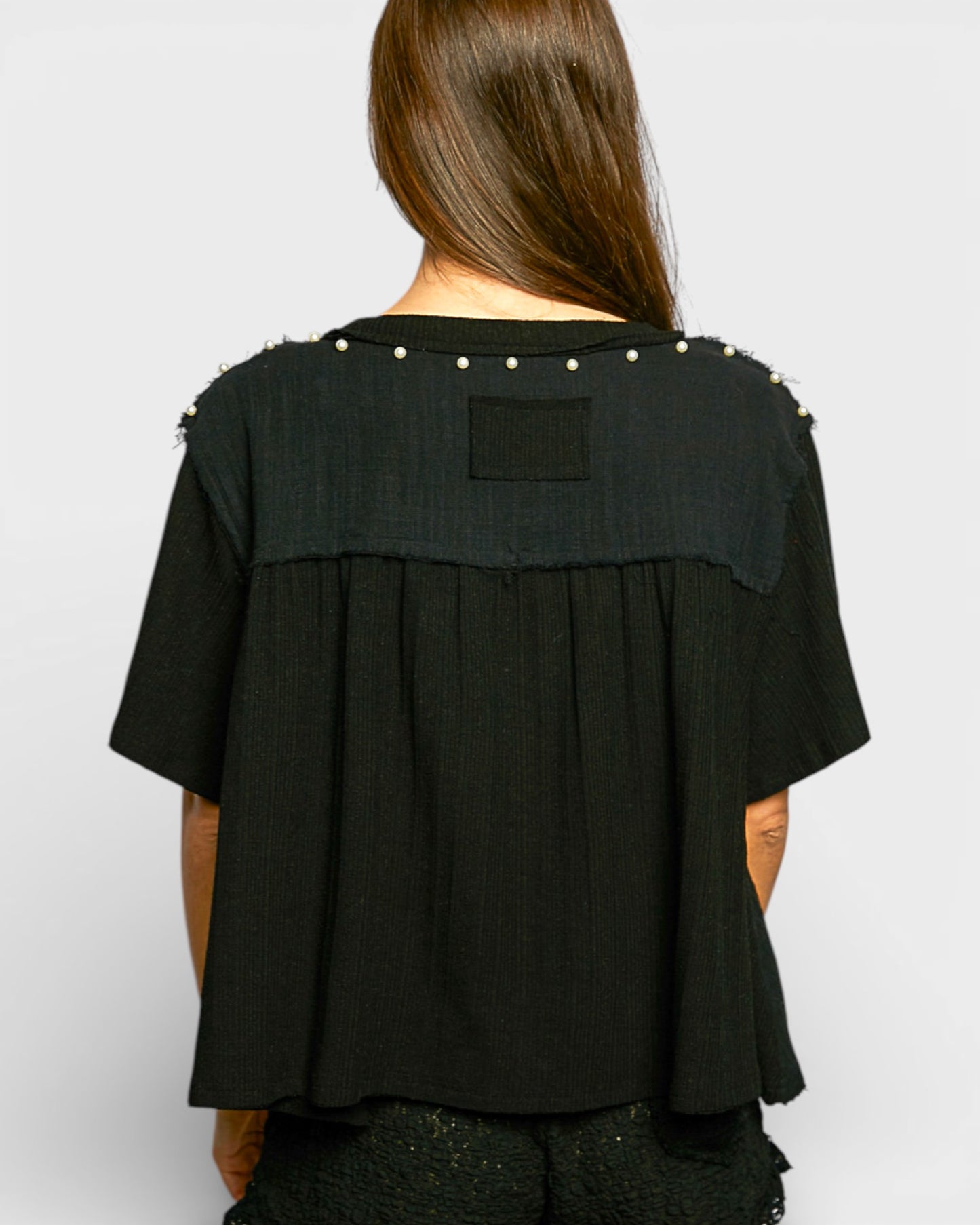 Black top with pearl embellishments on a plain background