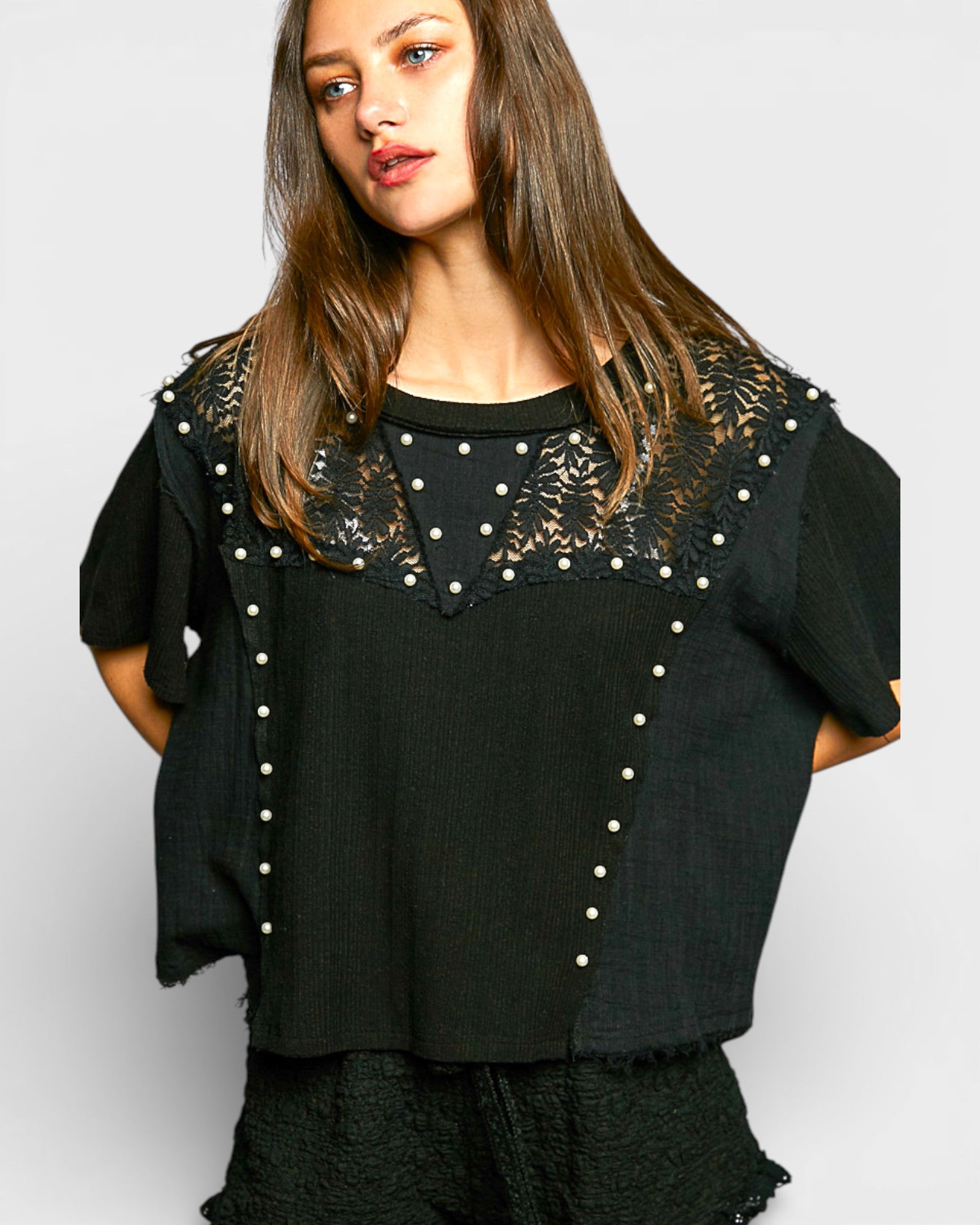 Woman wearing a black top with lace detailing on a white background