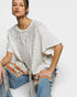 Woman wearing a white poncho with decorative buttons and patterned pants on a white background