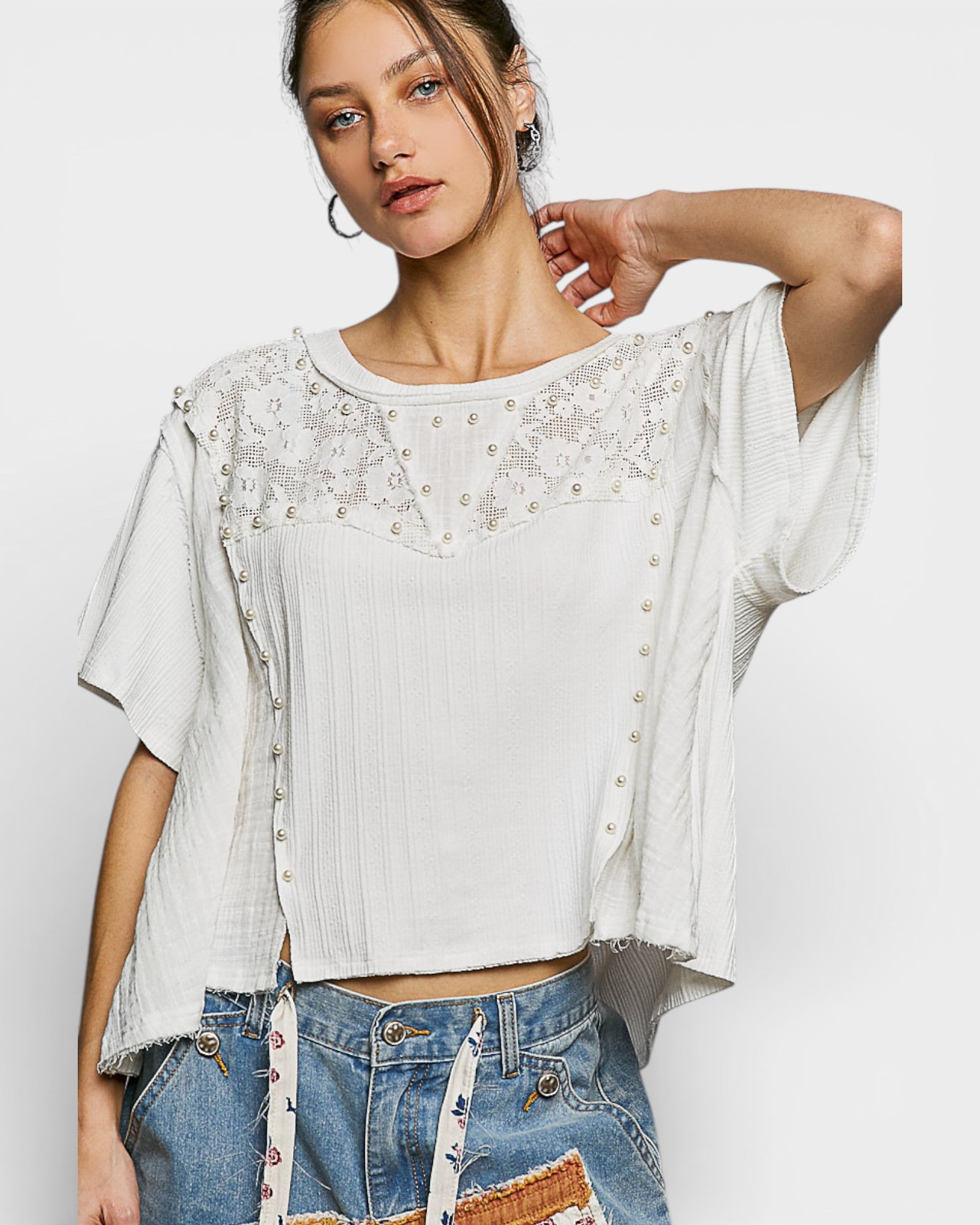 Woman wearing a white lace top and denim shorts on a plain background