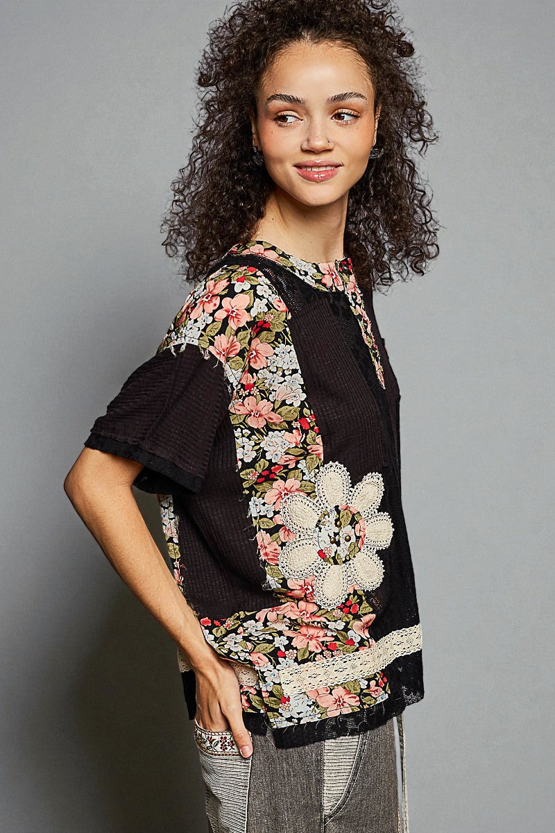 Woman wearing a black top with floral embroidery on a gray background