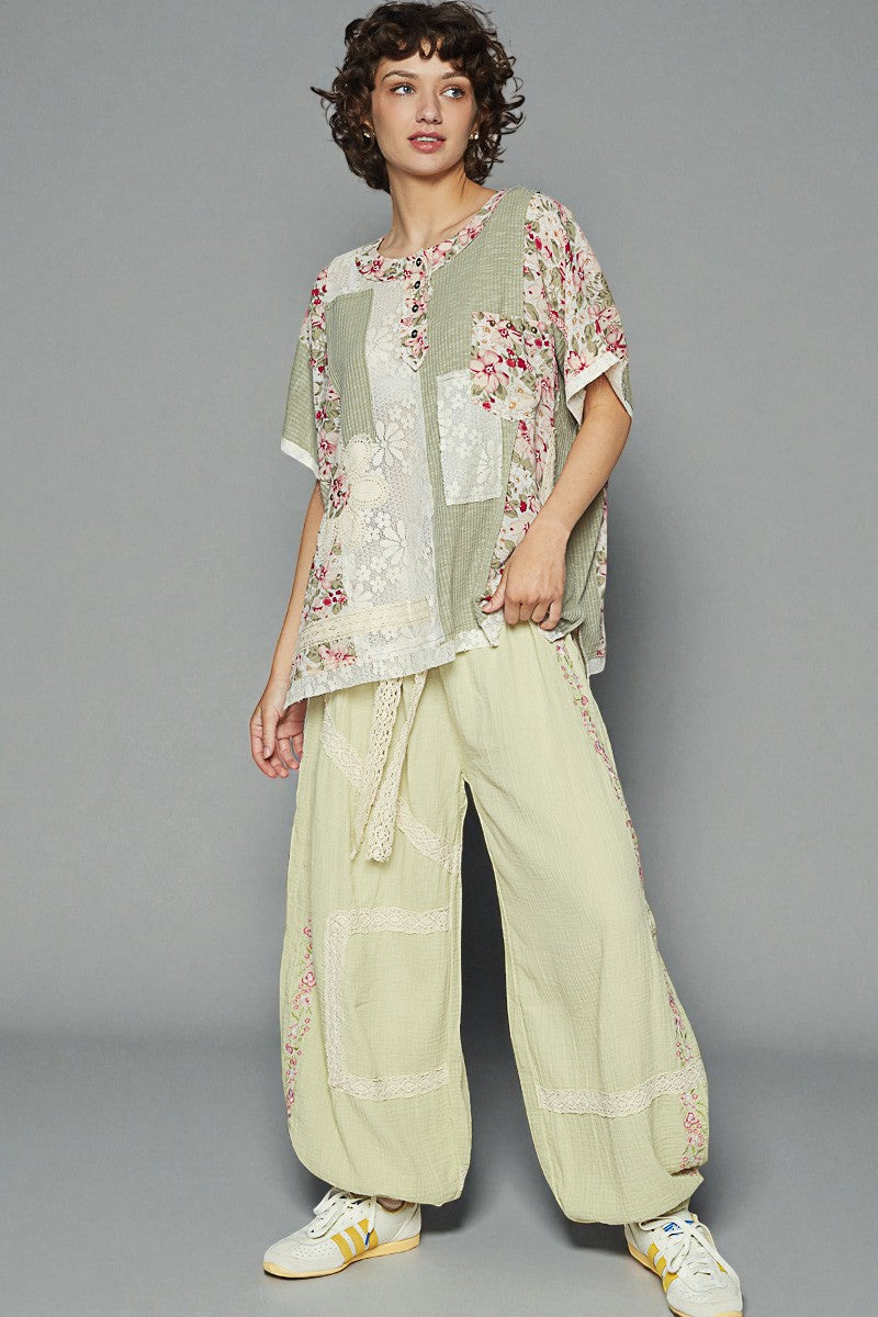 Woman wearing a floral top and light green pants against a gray background