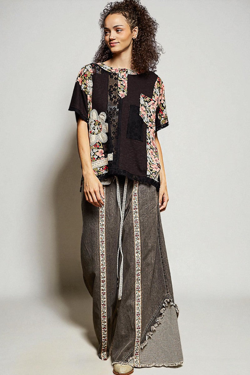 Woman wearing a floral top and gray pants with decorative trim against a plain background