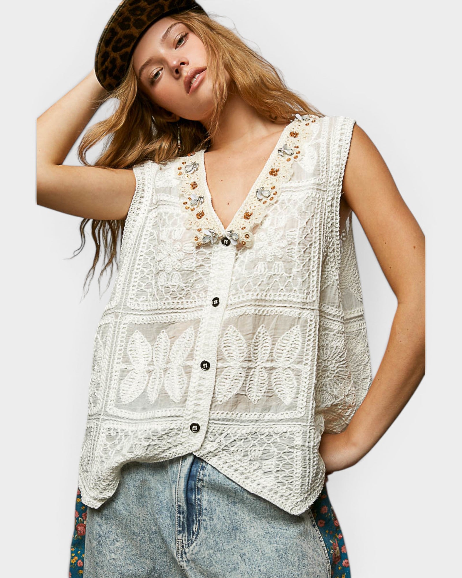 Woman wearing a white embroidered vest and jeans on a plain background