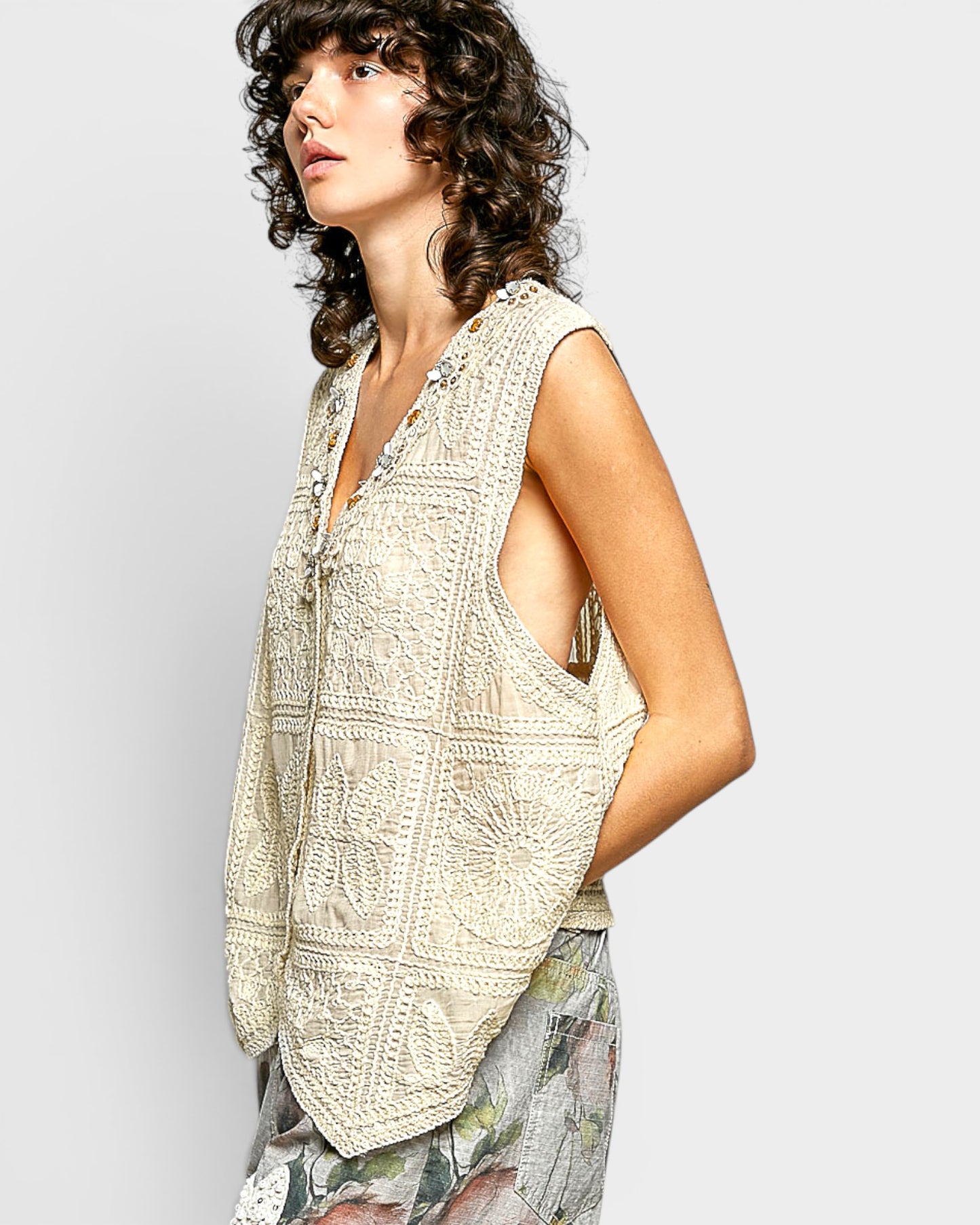 Woman wearing a beige patterned sleeveless top against a light gray background