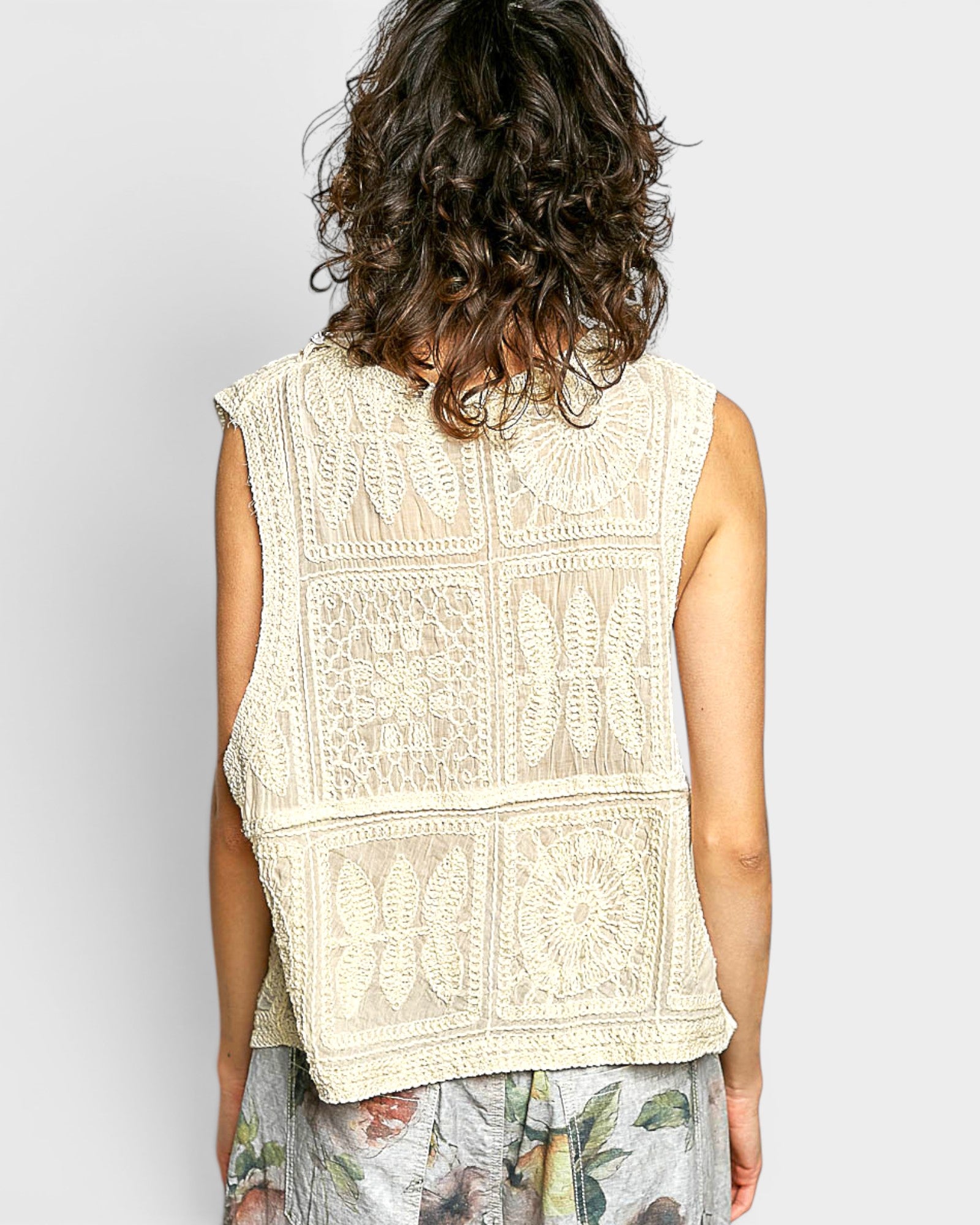 Person wearing a beige embroidered sleeveless top against a plain background