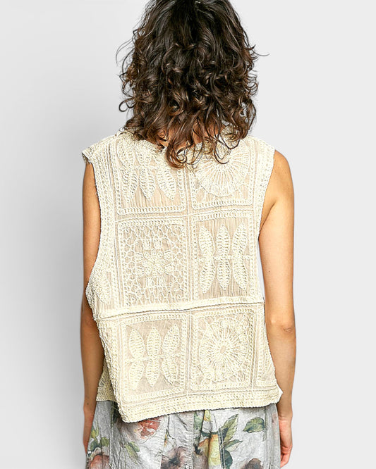 Person wearing a beige embroidered sleeveless top against a plain background