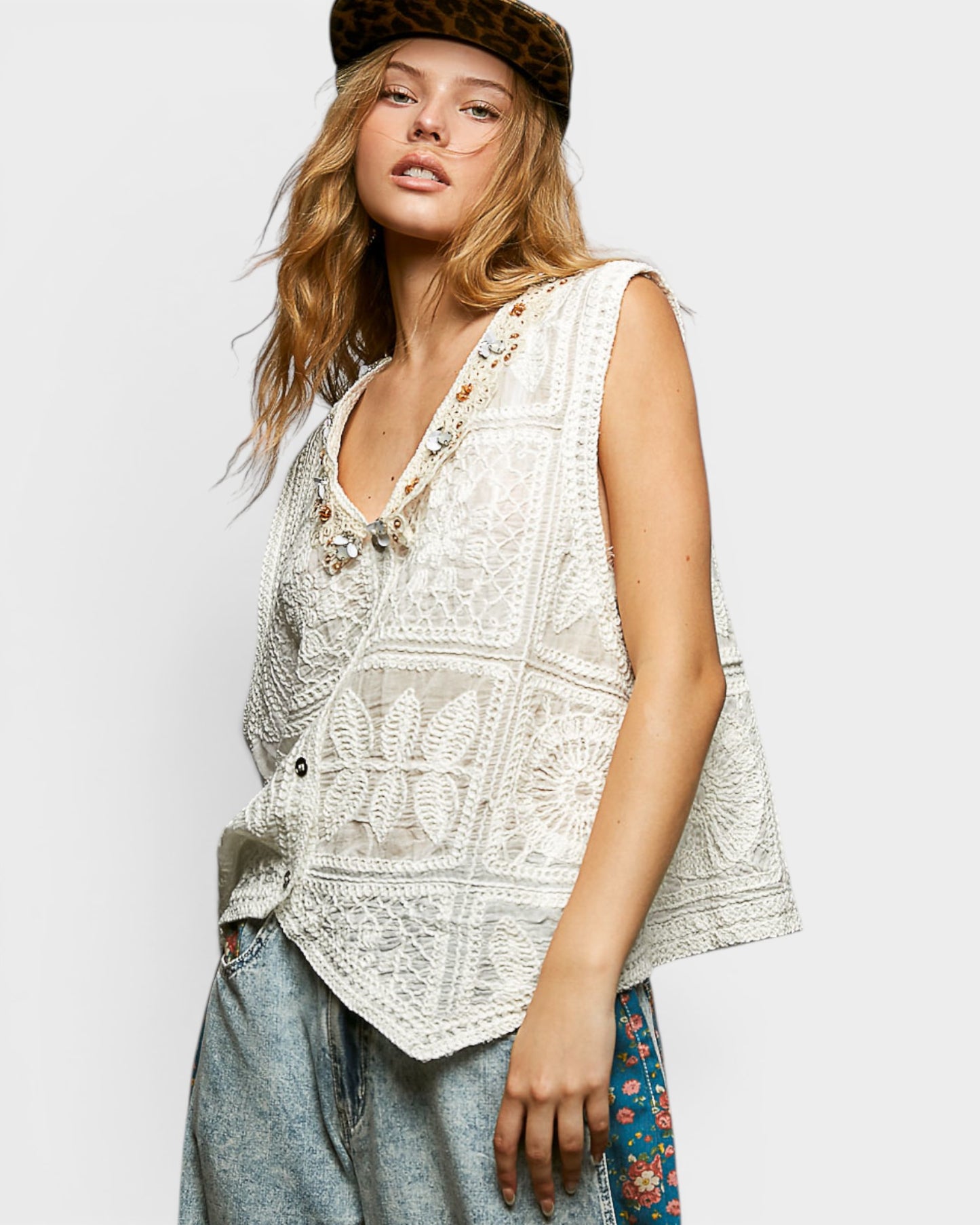 Woman wearing a sleeveless crochet top and jeans against a plain background
