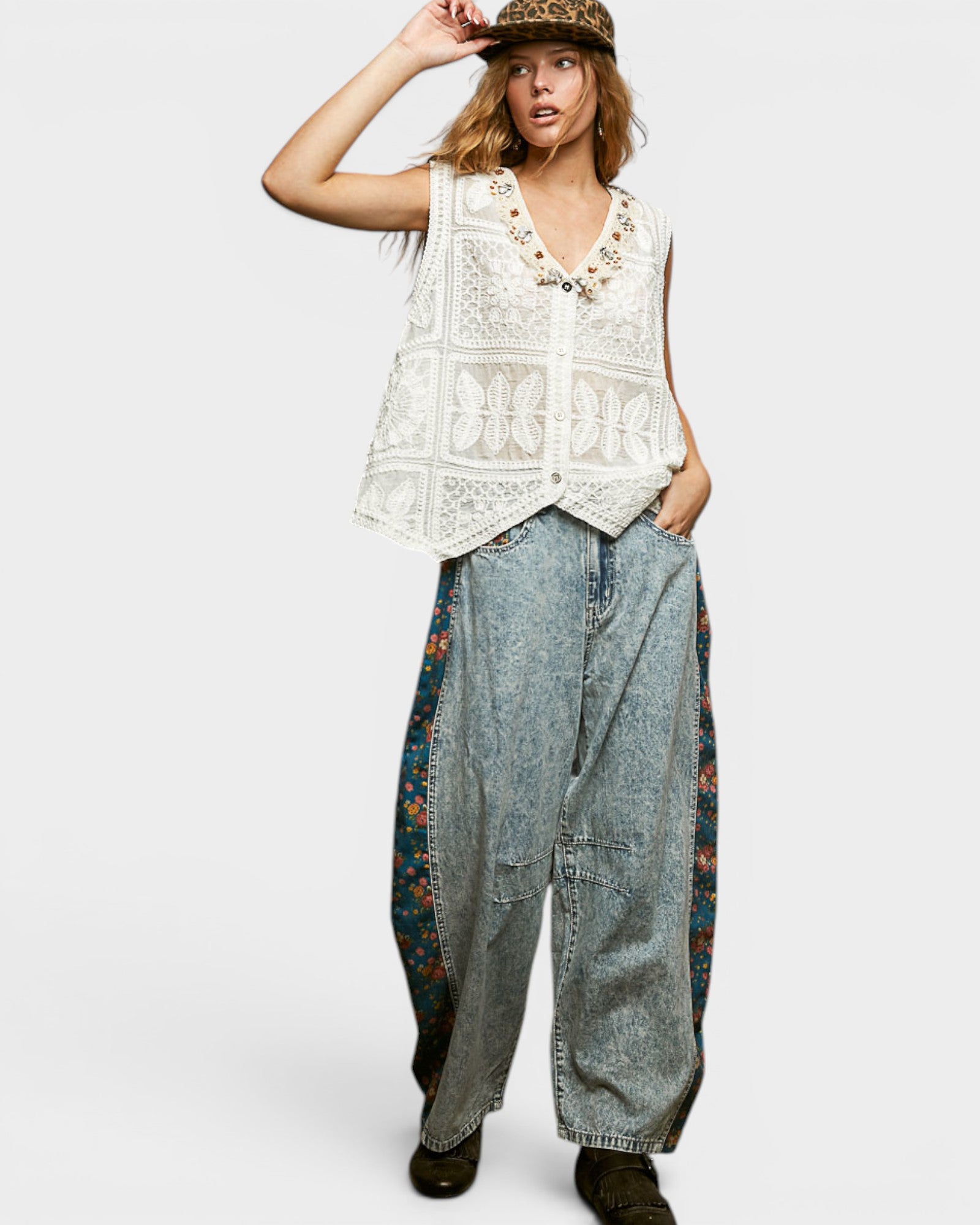 Woman wearing a white lace top and floral denim pants on a white background