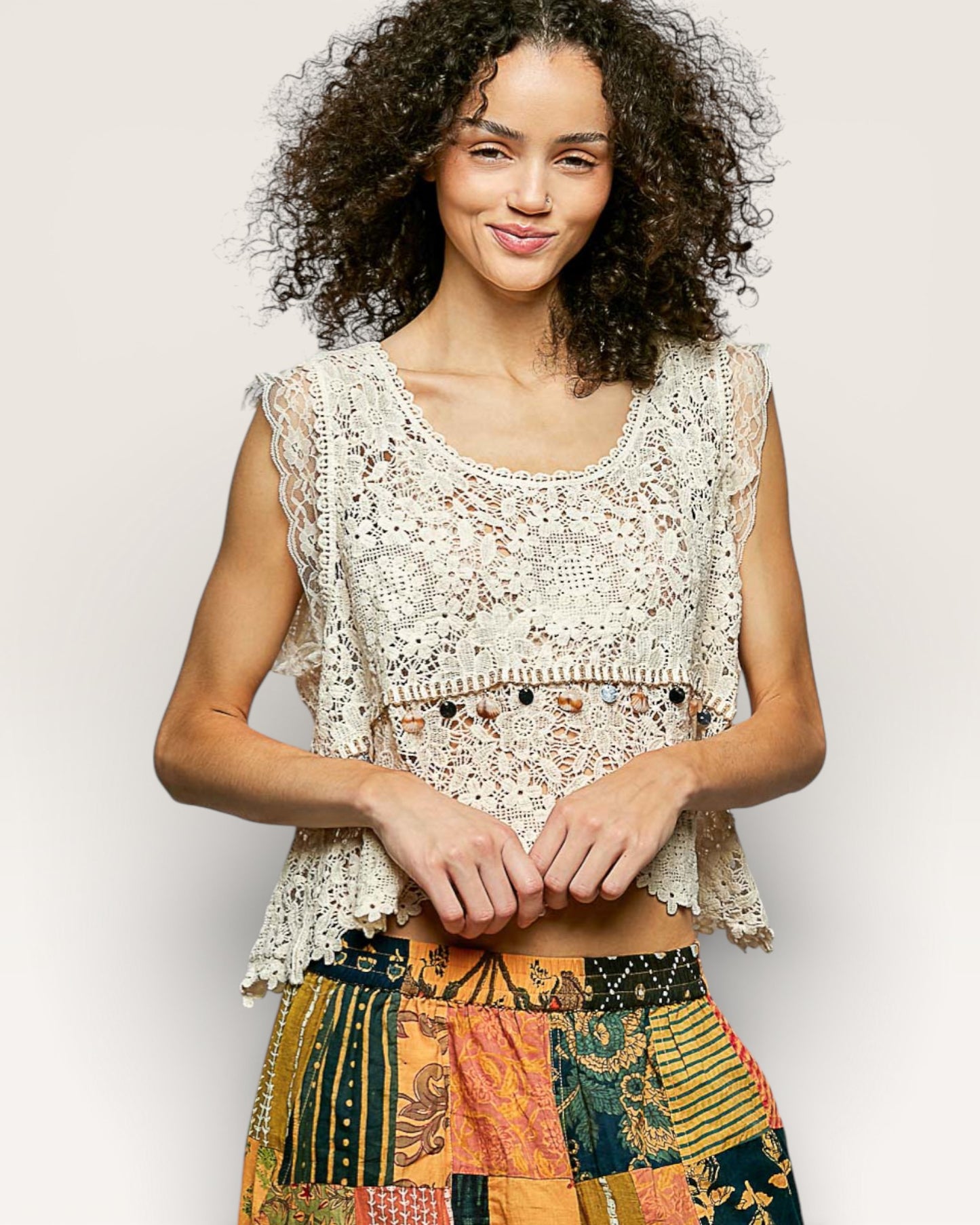 Woman wearing a lace top and colorful patchwork skirt against a plain background
