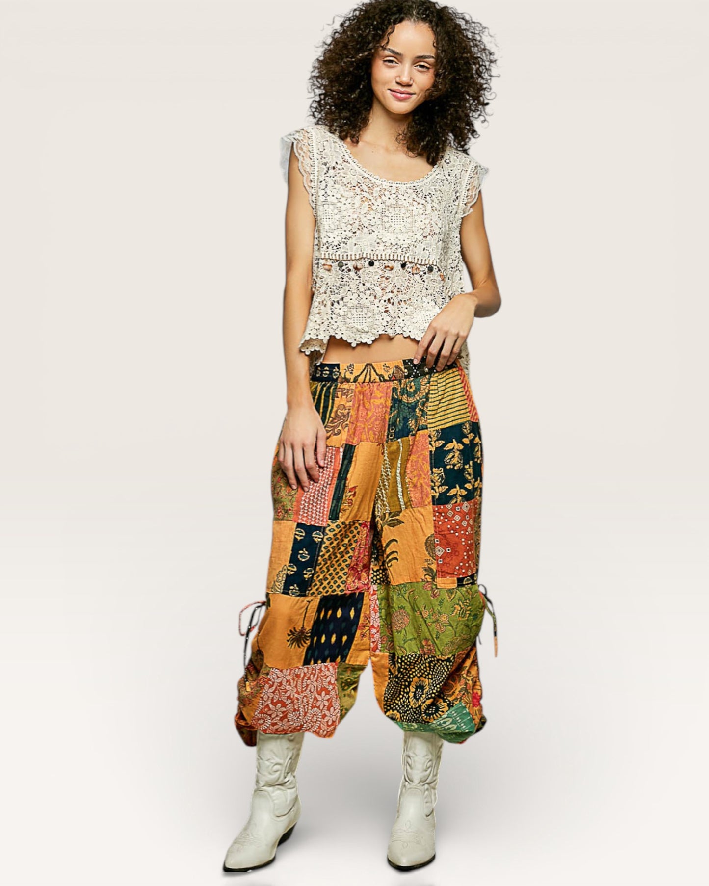 Woman wearing a sleeveless lace top and colorful patchwork pants on a white background