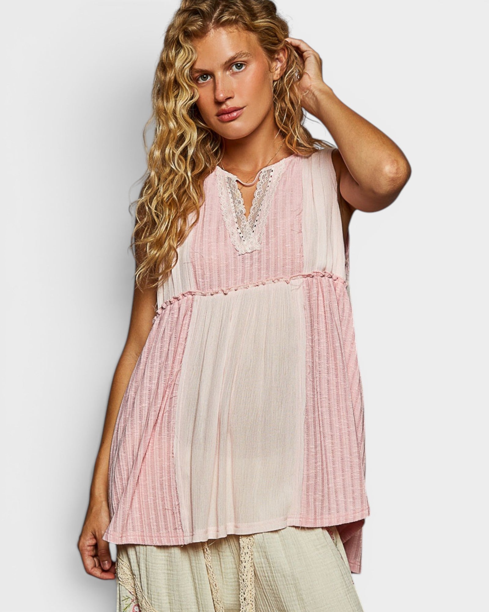 Woman wearing a sleeveless, layered top with pink and white patterns on a plain background