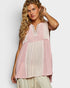 Woman wearing a sleeveless, layered top with pink and white patterns on a plain background