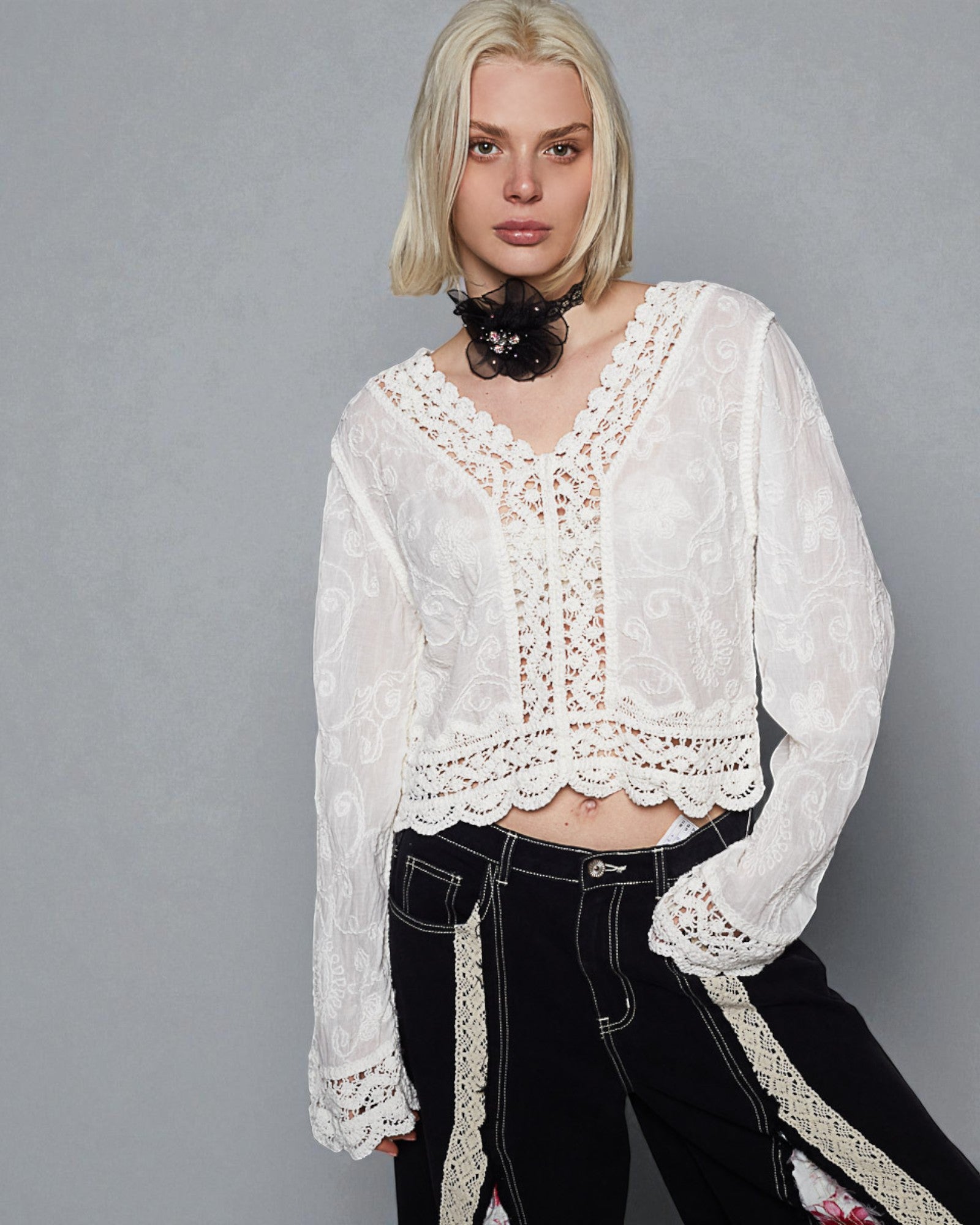Person wearing a white lace top and black pants against a gray background