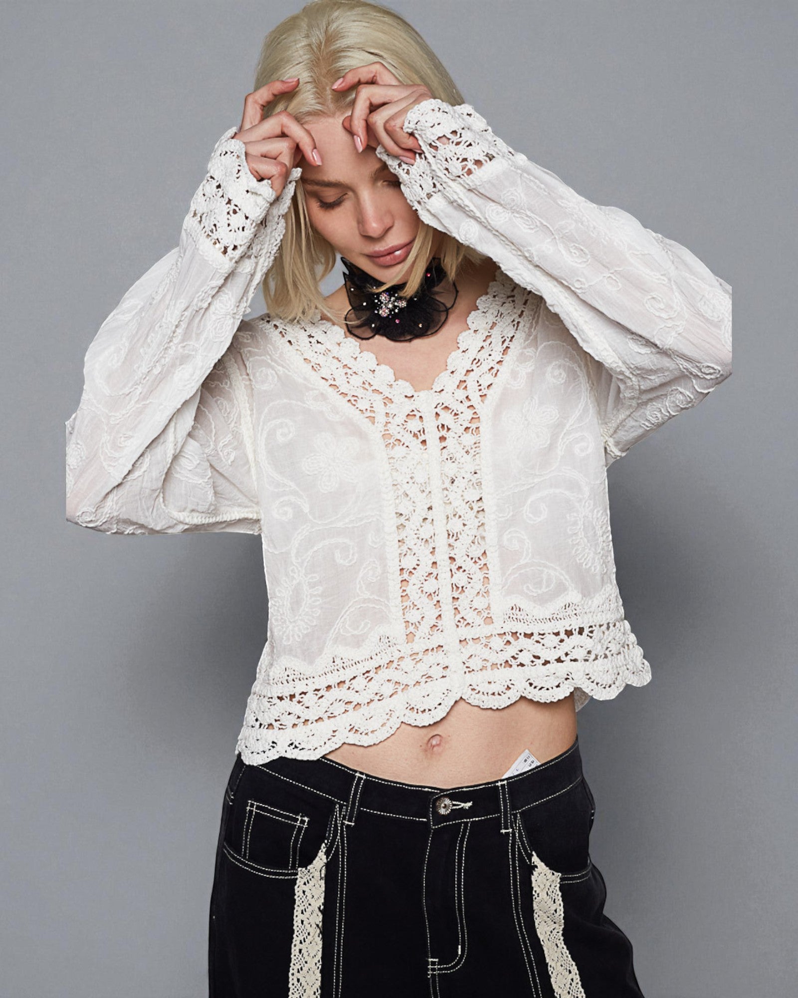 Person wearing a white lace top and black pants against a gray background