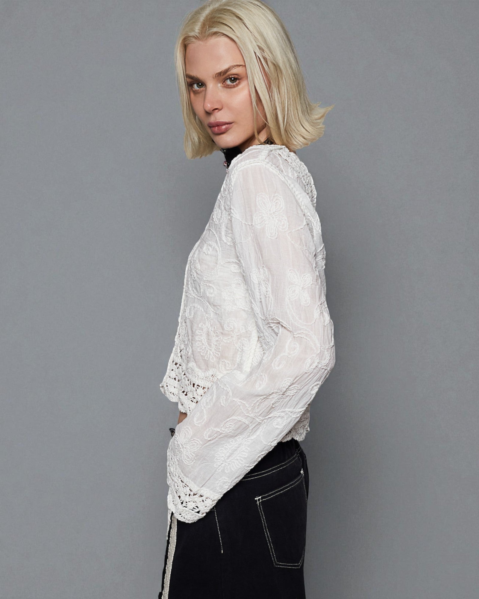 Woman wearing a white lace top against a gray background