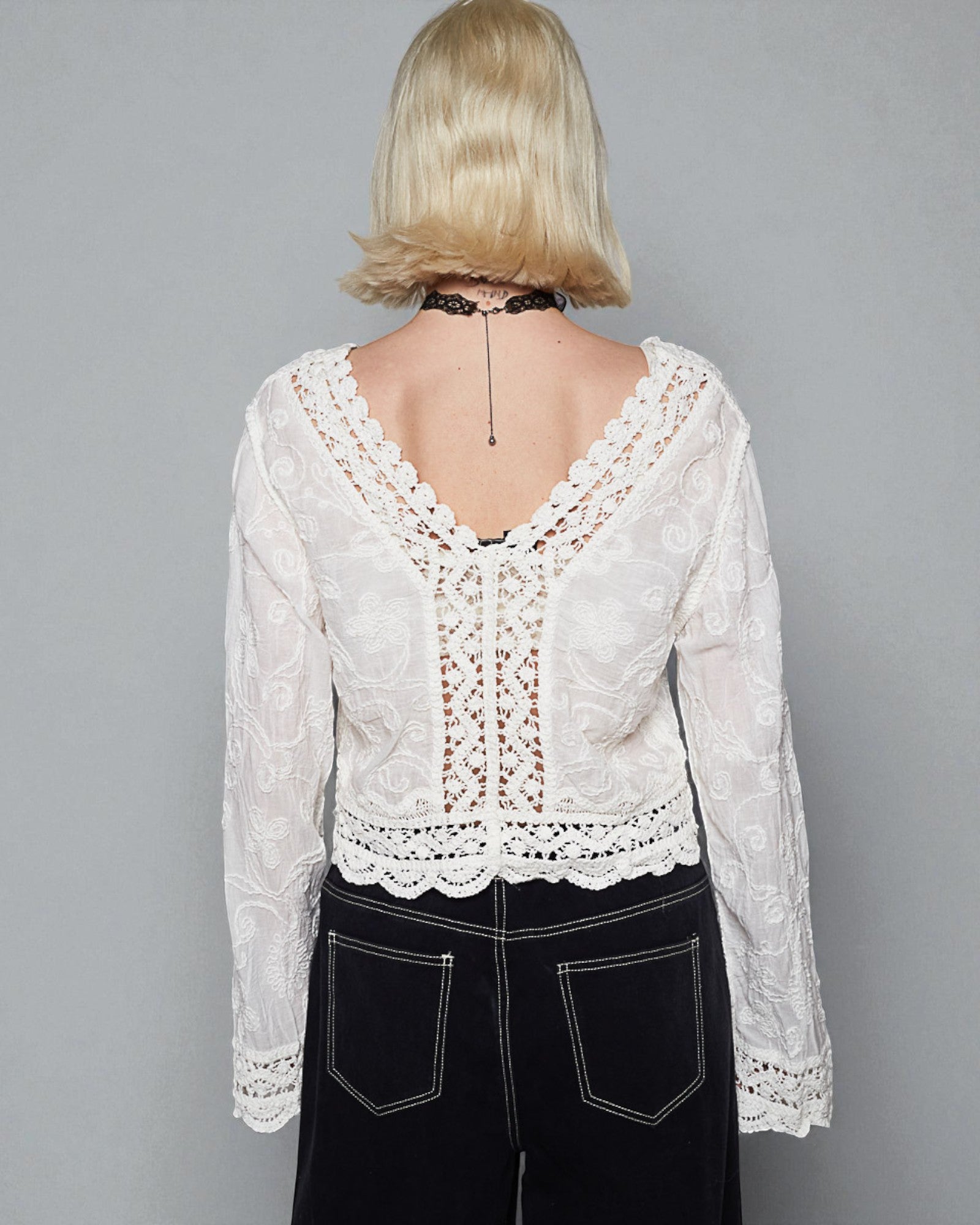 Person wearing a white lace top with a gray background