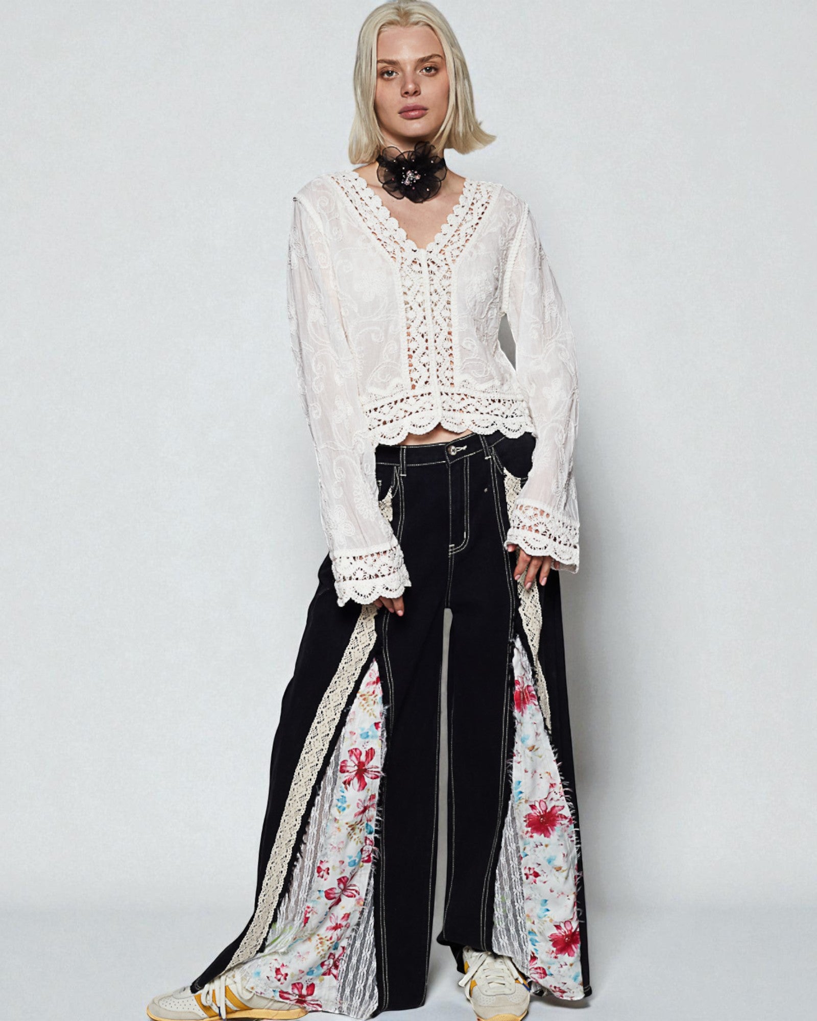 Woman wearing a white lace top and black pants with floral patterns on a plain background