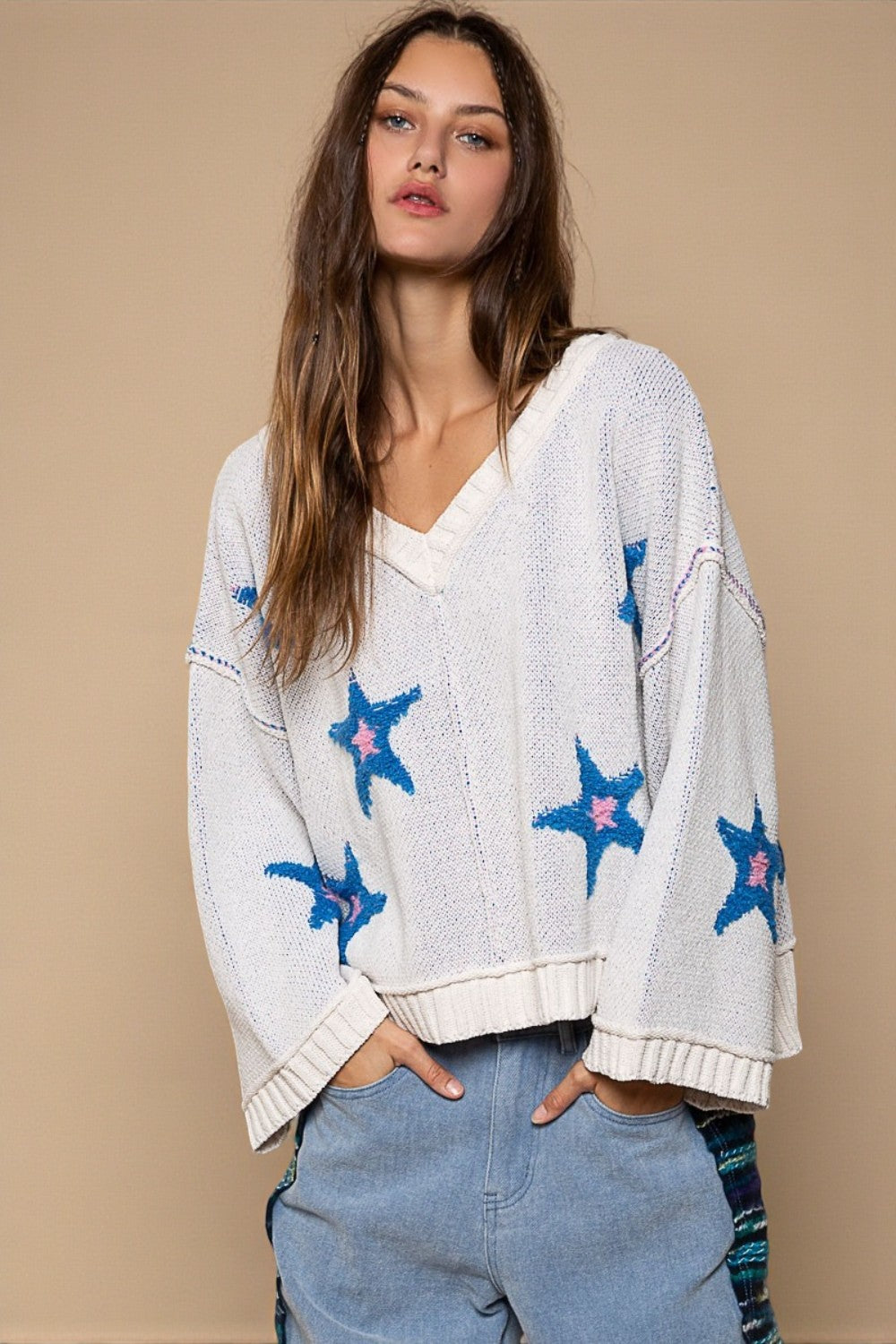 Woman wearing a white sweater with blue star patterns on a beige background