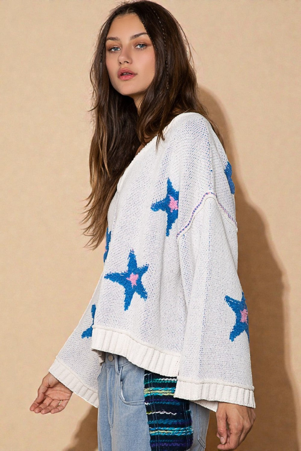 Woman wearing a white sweater with blue star patterns against a beige background