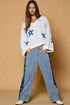 Woman wearing a white sweater with blue star patterns and blue jeans against a beige background