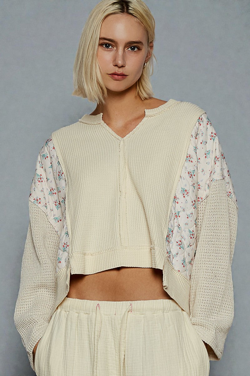 Woman wearing a beige outfit with floral sleeves against a gray background