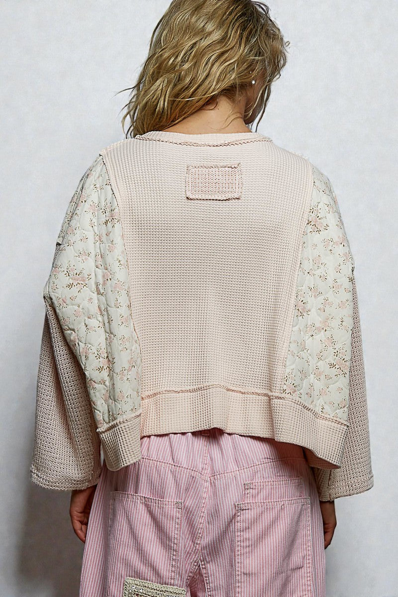 Person wearing a beige textured jacket with floral patterns and pink pants on a white background